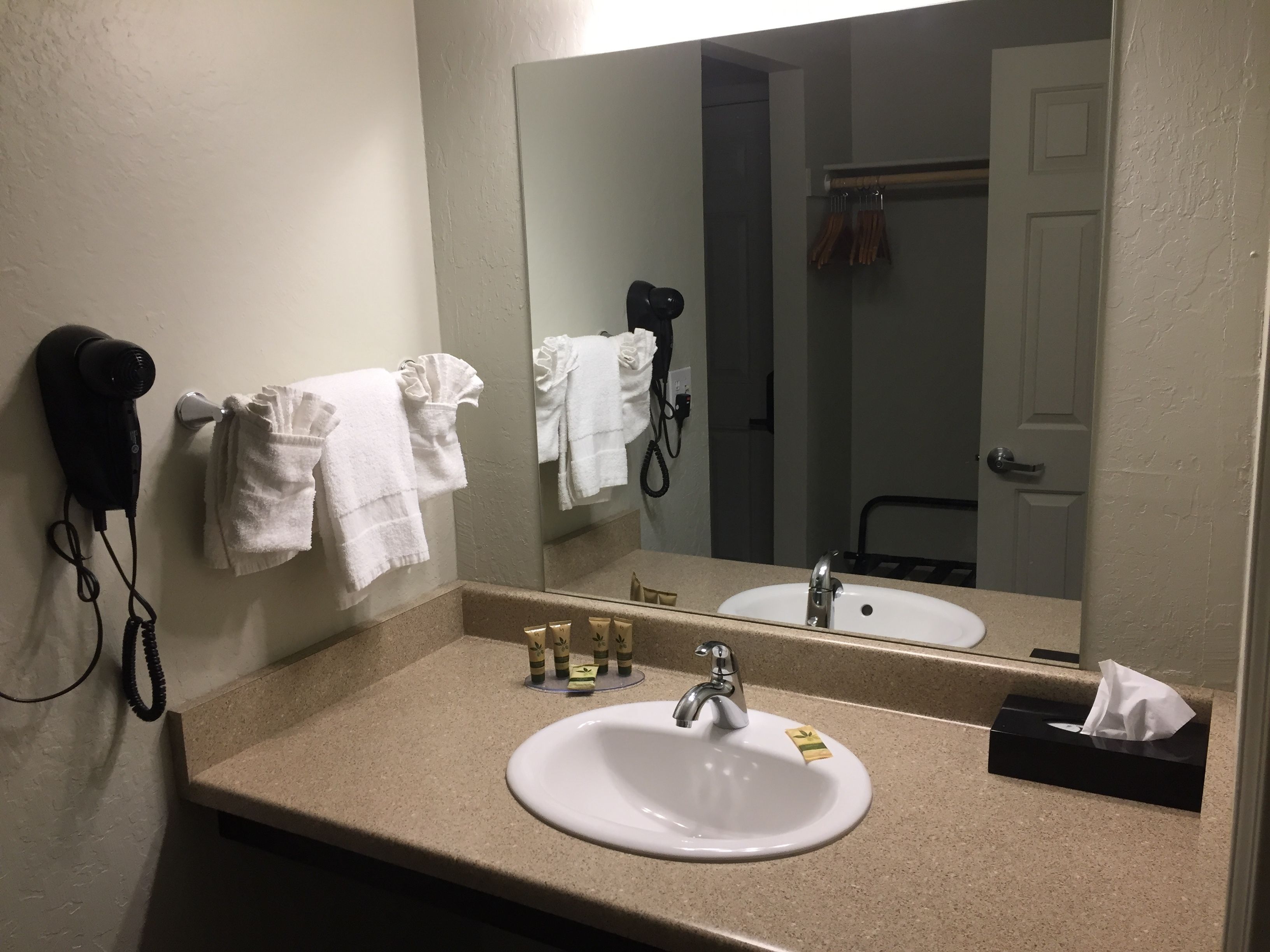 A bathroom with a sink, mirror, towel rack, hair dryer, and toiletries.