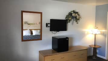 A hotel room with a bed, a dresser, a television, a wall-mounted mirror, a decorative wreath, and a floor lamp.