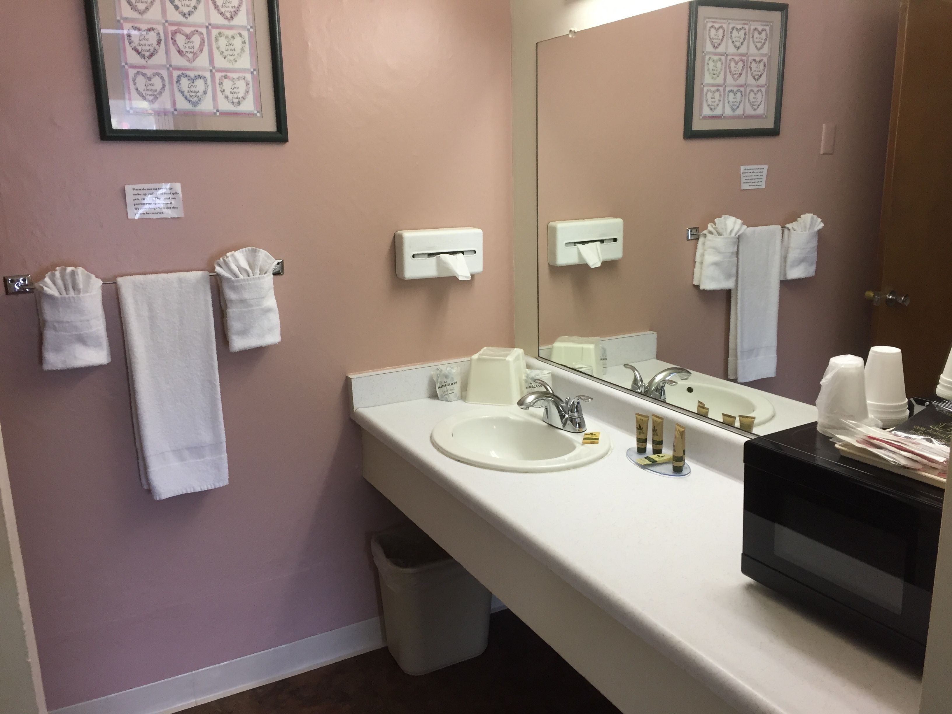 Un baño con lavabo, espejo, toallero y dispensador de desinfectante de manos.