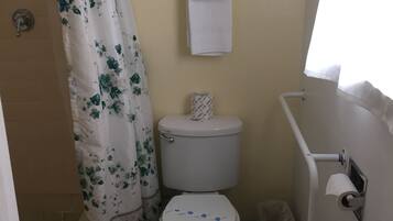 A bathroom with a toilet, a shower curtain, a towel rack, and a trash bin.