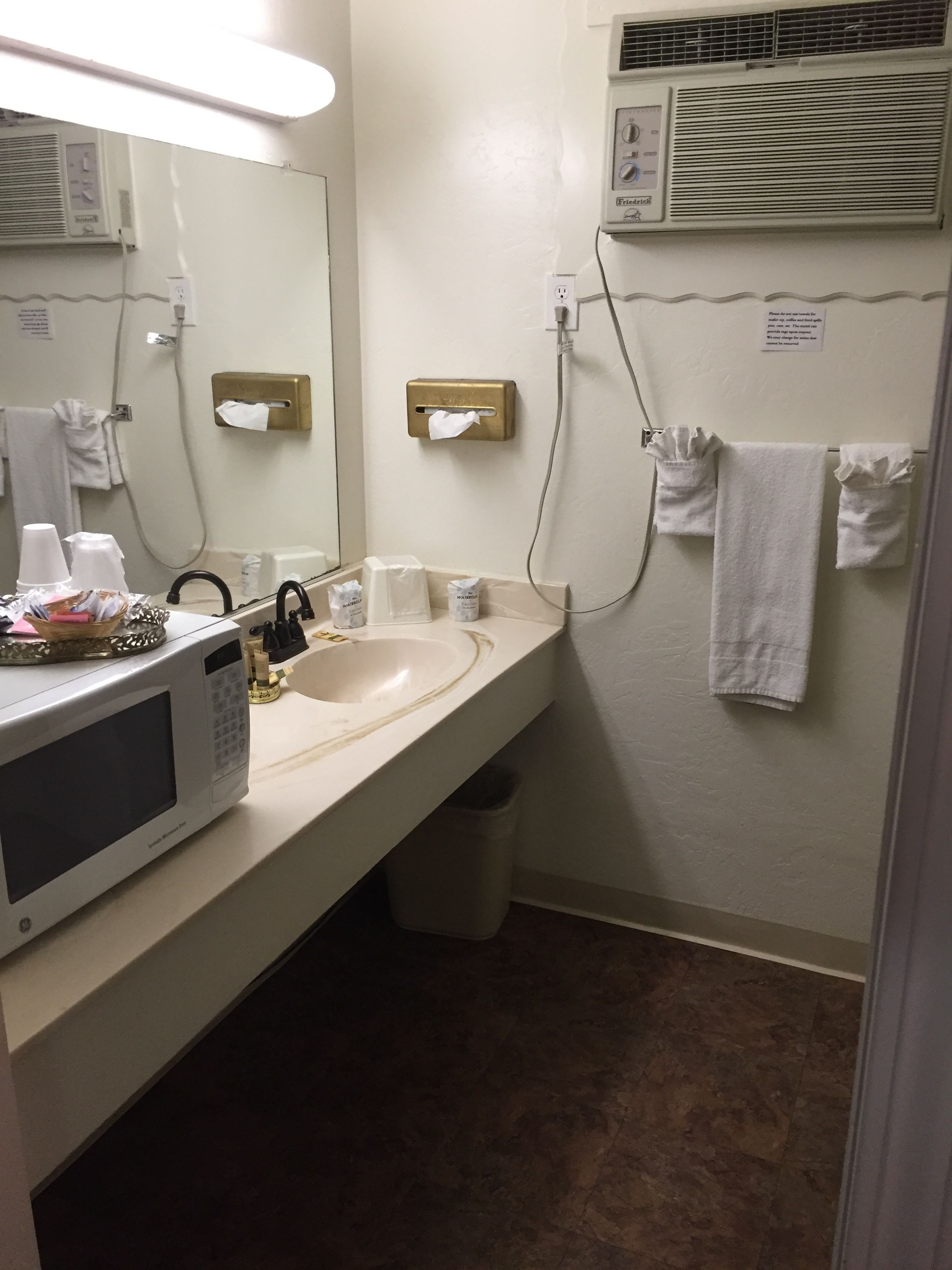 A bathroom with a sink, mirror, microwave, towel rack, and hand dryer.