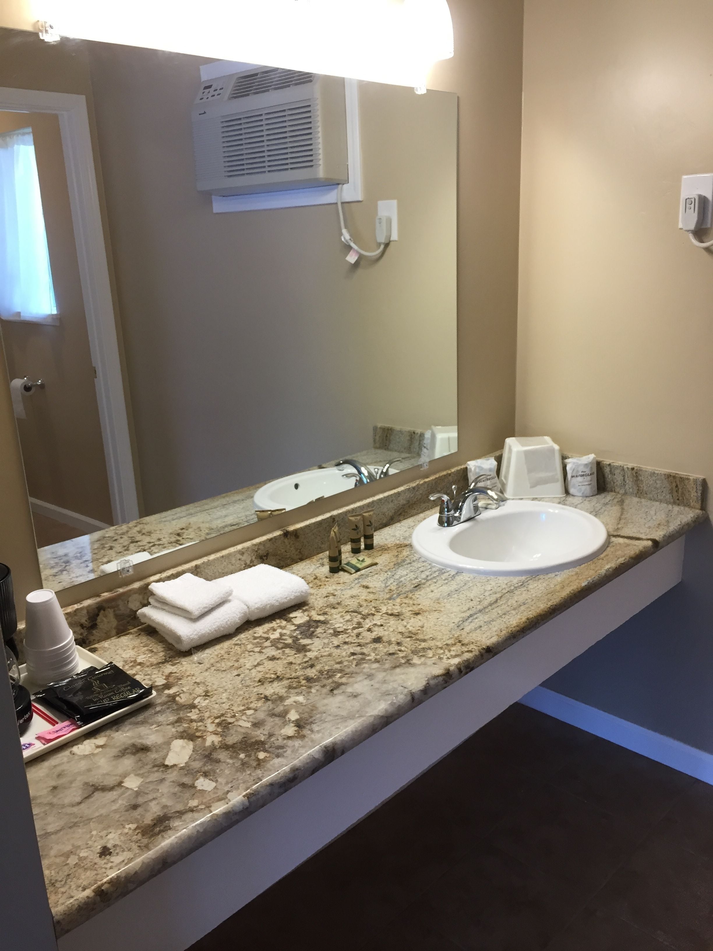 A bathroom with a granite countertop, two sinks, a large mirror, and a towel rack.