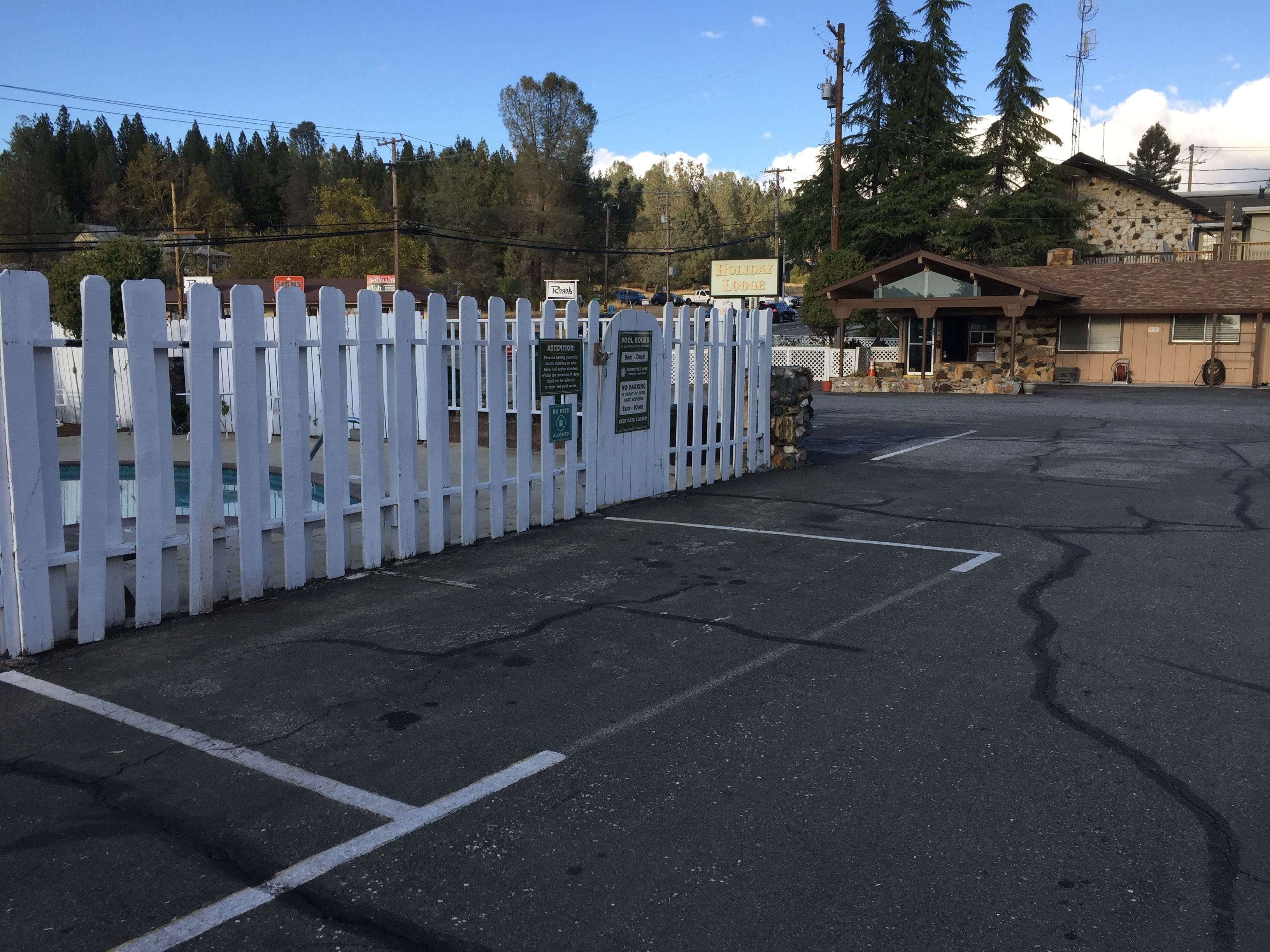 Un parcheggio con una recinzione in legno bianco, un edificio in pietra e un cartello per Holiday Lodge.