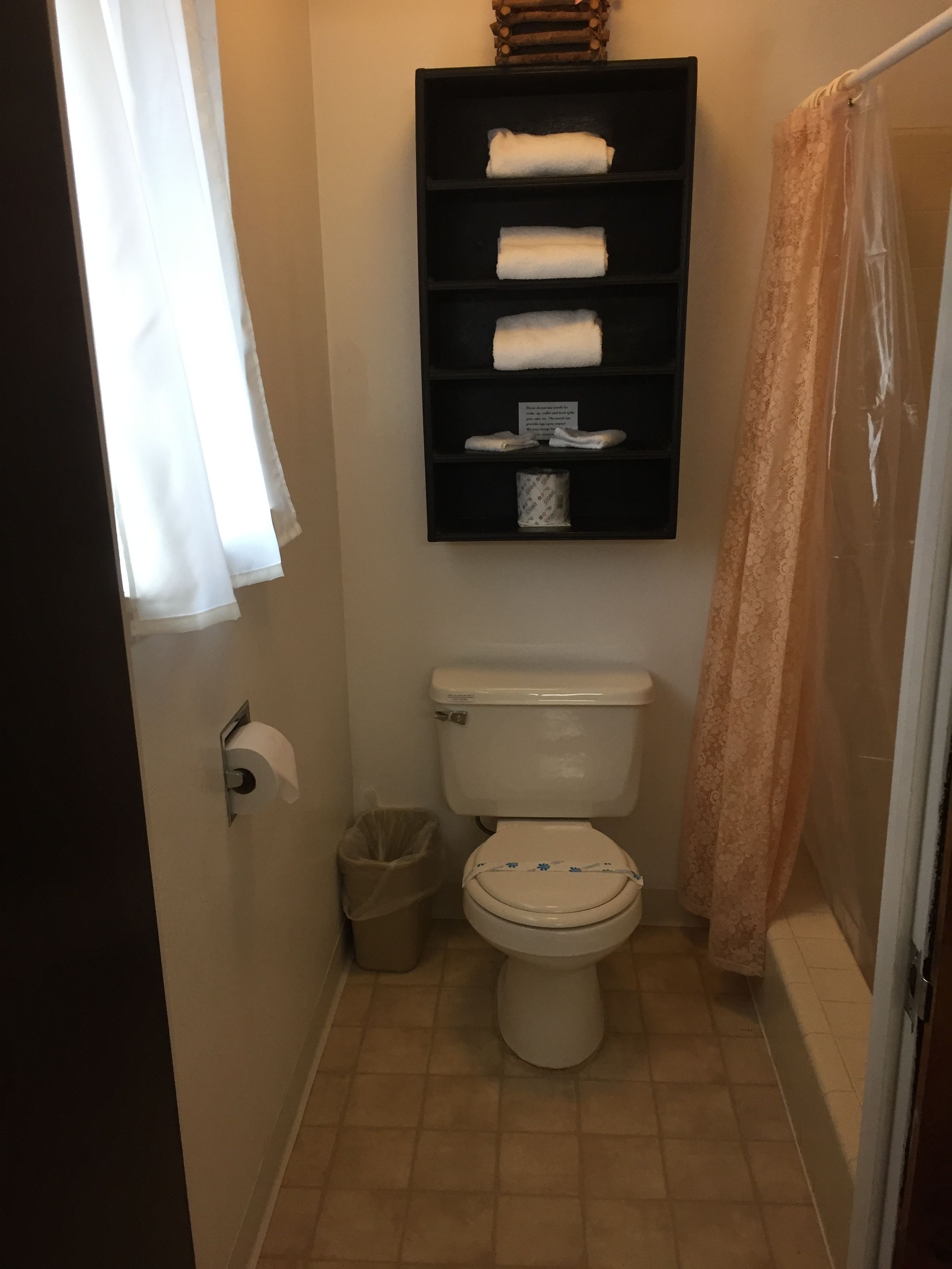 Un baño pequeño con inodoro, un estante con toallas, un cubo de basura y una cortina de ducha.