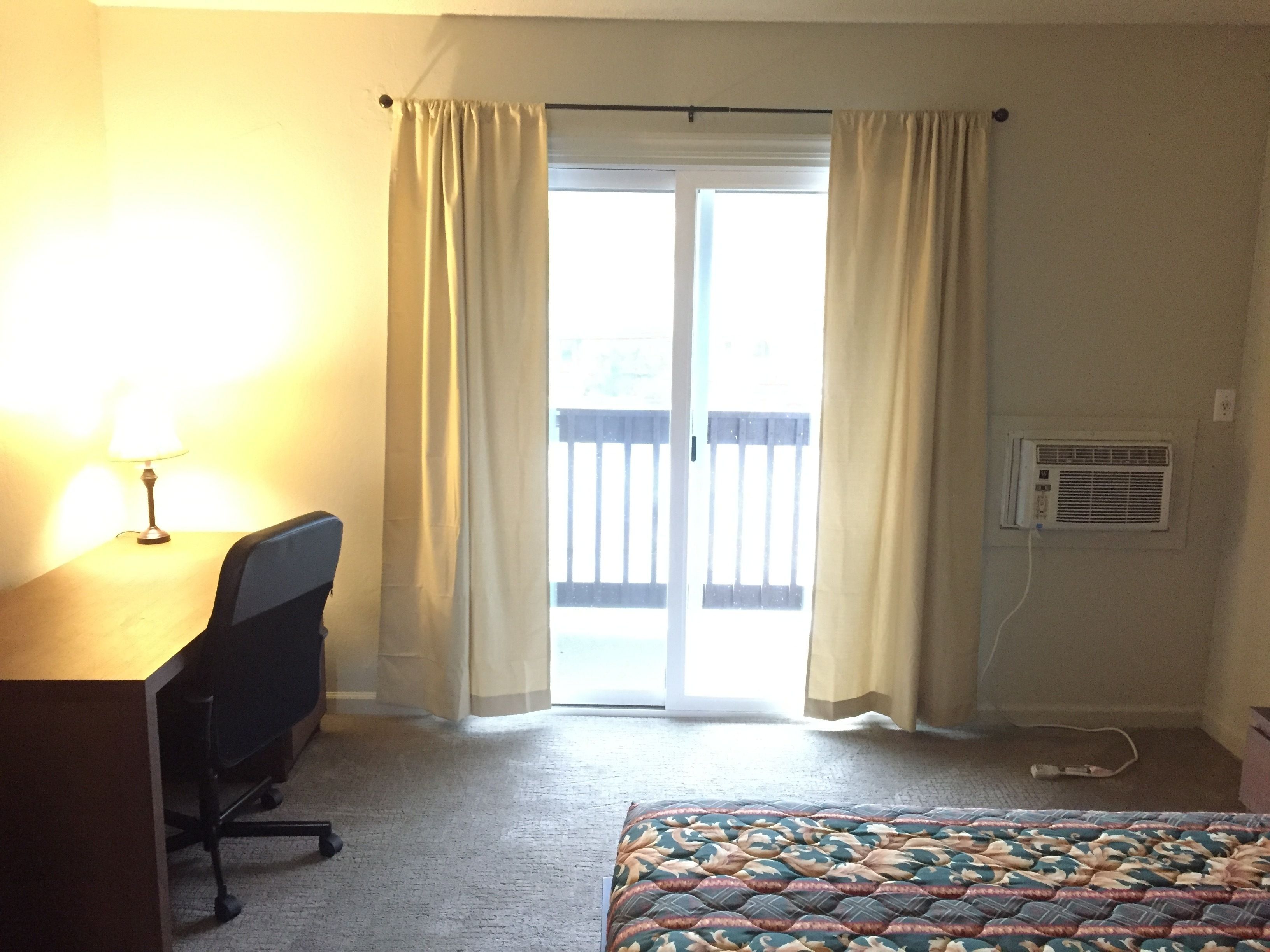 A hotel room with a desk, chair, bed, and a sliding door to the outside.