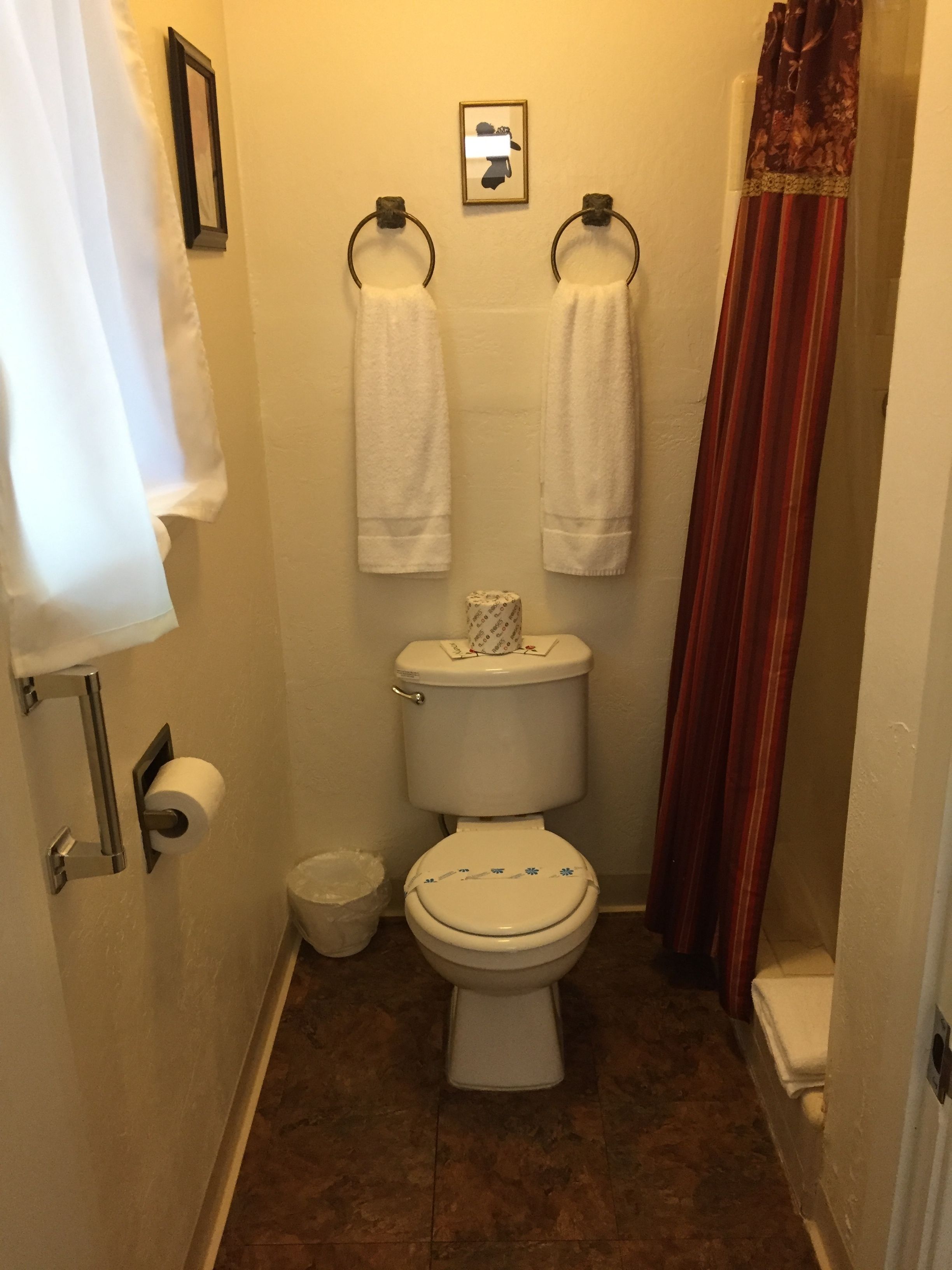 Un baño pequeño con un inodoro, dos toalleros, un dispensador de papel higiénico y una cortina de ducha.