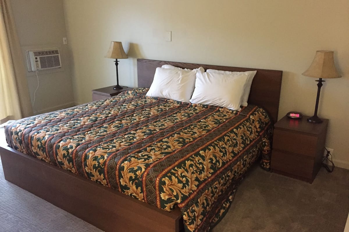 A neatly made bed with a patterned bedspread, two bedside lamps, and a nightstand with a clock.