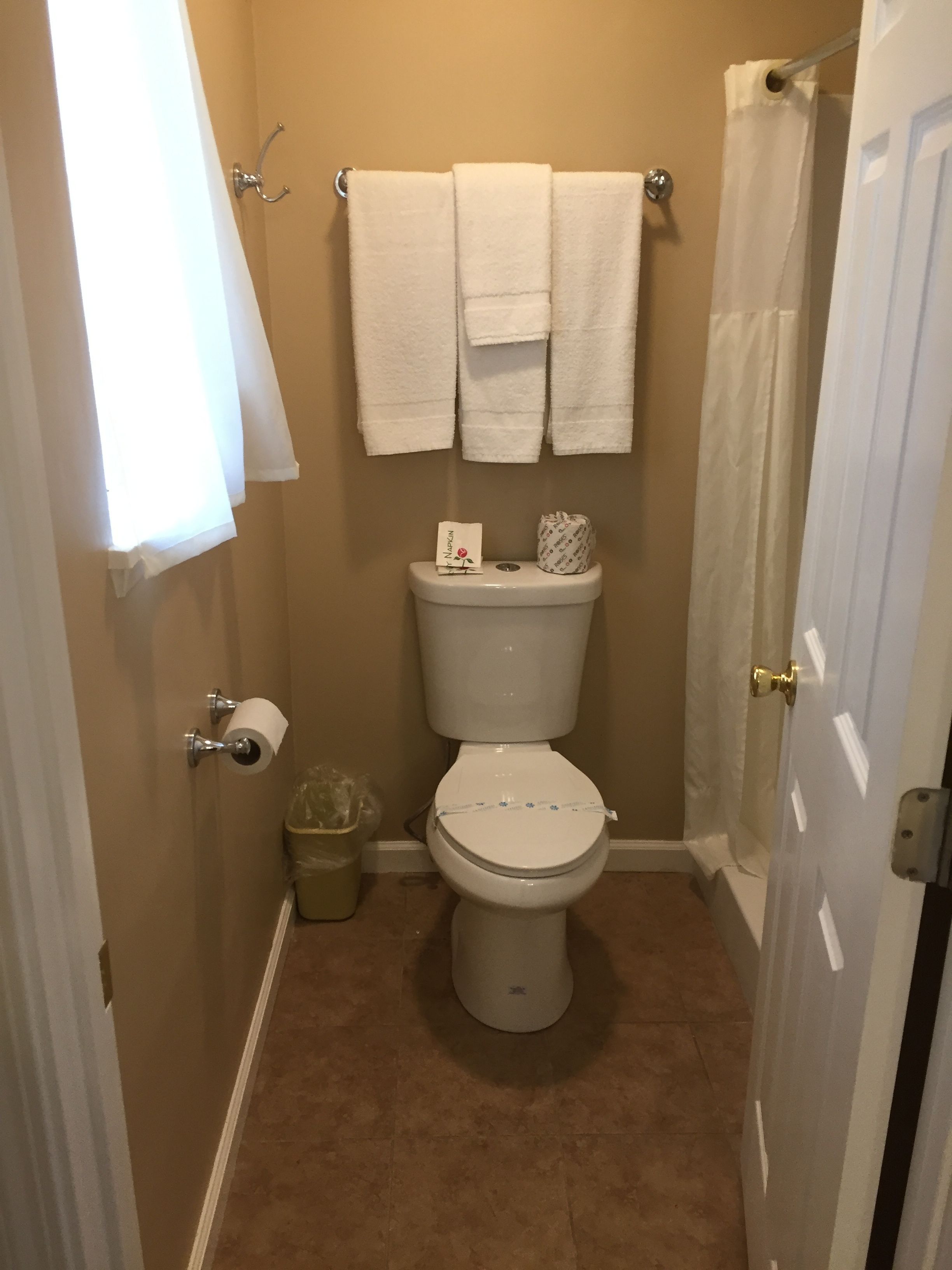 Een kleine, schone badkamer met toilet, twee witte handdoeken aan een rek, een rol toiletpapier en een kleine prullenbak.