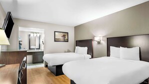 A hotel room with two beds, a desk, a chair, a TV, a bathroom, and a painting on the wall. - Rodeway Inn Waco Downtown near University (Waco)