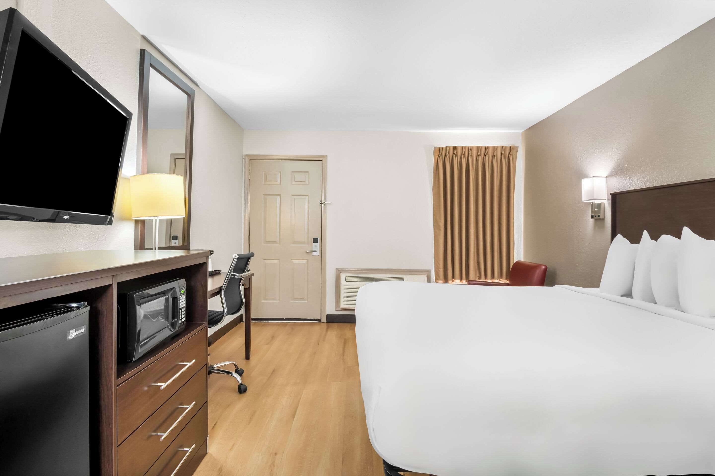Une chambre d’hôtel équipée d’un lit, d’une télévision, d’un bureau avec un micro-ondes, d’une chaise et d’une porte.