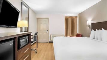Une chambre d’hôtel équipée d’un lit, d’une télévision, d’un bureau avec un micro-ondes, d’une chaise et d’une porte.