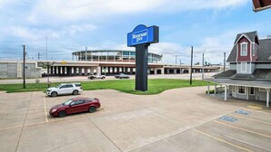 A parking lot with a sign for Rodeway Inn, a building with a glass facade, and a red car parked in the lot. - Rodeway Inn Waco Downtown near University (Waco)