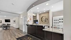 Un espace d’accueil comprenant un comptoir de réception, un écran numérique, une machine à café fixée au mur et un présentoir de tasses.