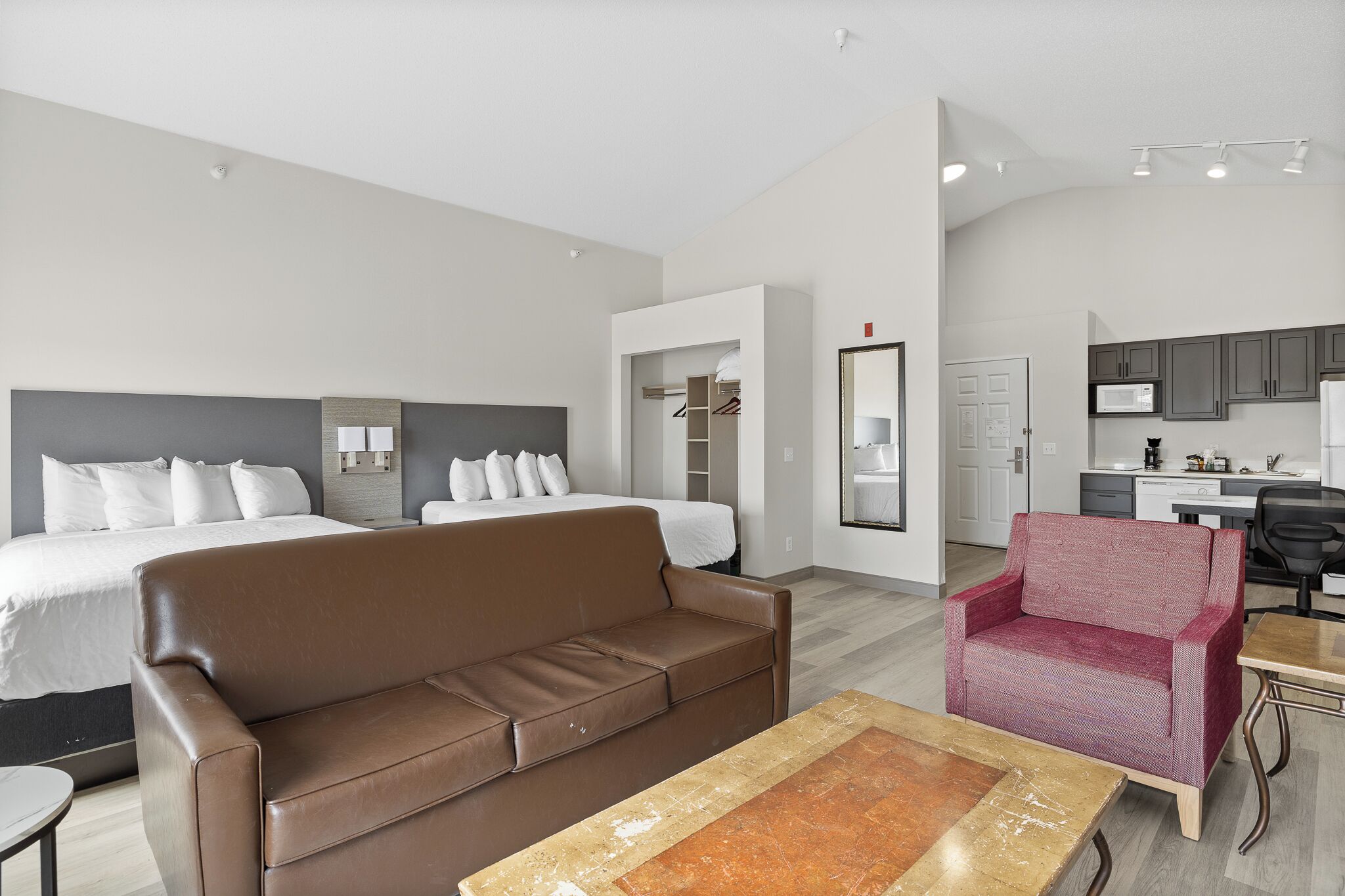 Una habitación de hotel moderna con una cama, un sofá marrón, un sillón rojo y una mesa de comedor.