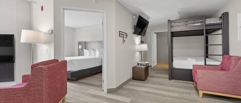 A hotel room with a bunk bed, a desk with a chair, a flat-screen TV, and a lamp.