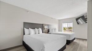 Une chambre d’hôtel avec deux lits, une grande fenêtre, un téléviseur à écran plat et un luminaire fixé au plafond.
