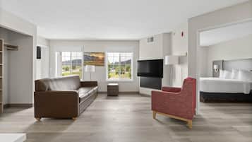 Una sala de estar moderna con un sofá marrón, un sillón rojo, un televisor de pantalla plana y una cama con ropa blanca.