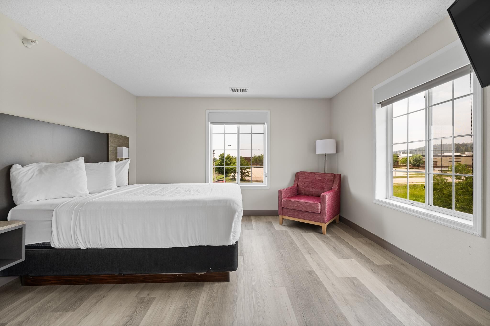 A modern bedroom with a large bed, a red chair, and a view of the outdoors through a window.