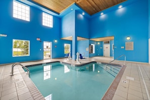 An indoor swimming pool with blue walls and a wooden ceiling, featuring clear windows, a lifeguard chair, and a pool ladder. - GrandStay Residential Suites - Rapid City (Rapid City)