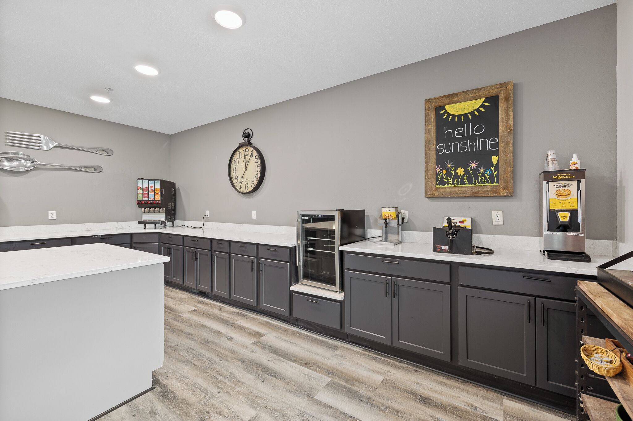 A modern kitchen with grey cabinets, a white countertop, a clock, a coffee machine, and a wall clock.