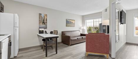 A modern kitchen with a dining area, a sofa, and a TV mounted on the wall.