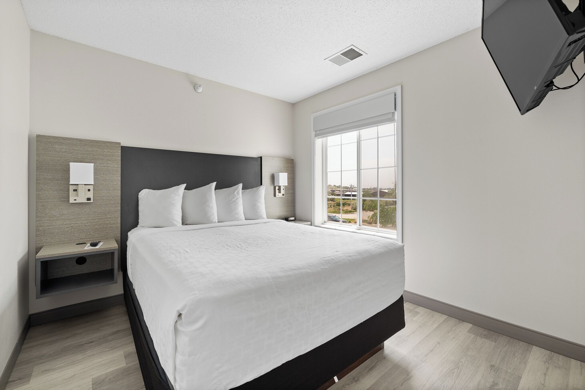 Een moderne hotelkamer met een groot bed, een nachtkastje, een aan de muur bevestigde televisie en een raam met uitzicht op de stad.