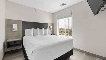 Quarto de hotel moderno com uma cama grande, uma mesa de cabeceira, uma TV na parede e uma janela com vista para a cidade.