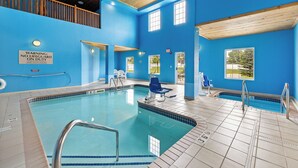 Une piscine intérieure aux murs bleus et au plafond en bois, équipée de chaises de sauveteur et d’un panneau d’avertissement.