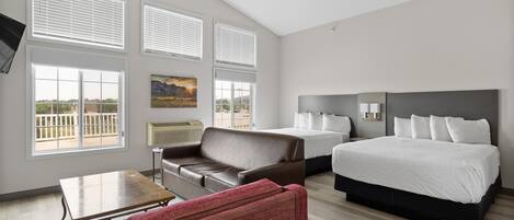 A hotel room with two beds, a sofa, a table, and large windows.