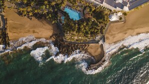 Vue aérienne d’un complexe hôtelier doté d’une piscine entourée de palmiers et donnant sur une plage.