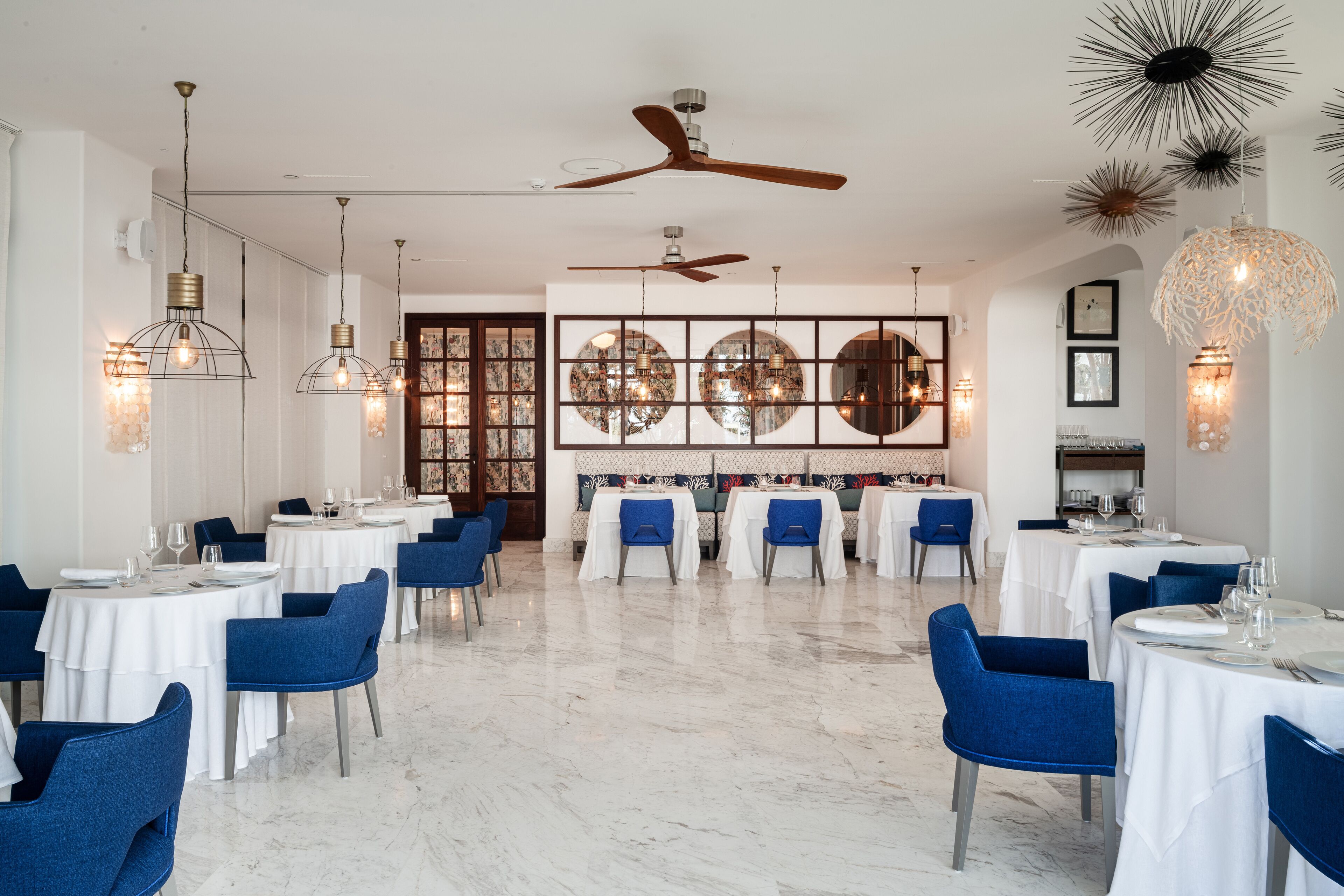 A spacious dining area with multiple tables and chairs, ceiling fans, and decorative lighting fixtures.