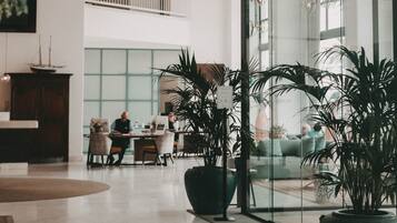 A spacious lobby with modern pendant lighting, large potted plants, and a seating area with a glass wall offering views of the interior.