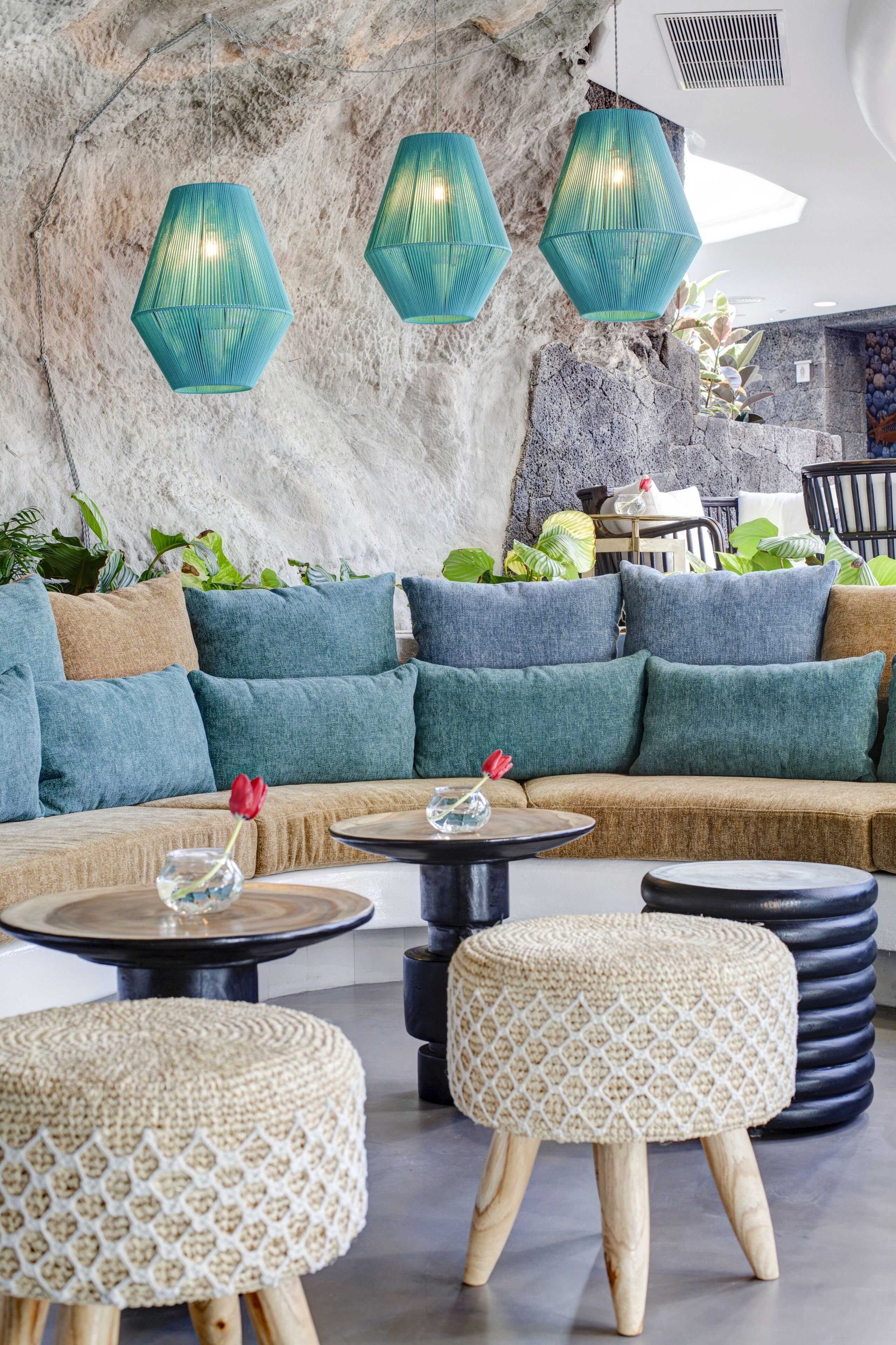 Ein moderner Lounge-Bereich mit einer Steinwand, einem beigen Sofa mit blauen Kissen und einem runden Tisch mit einer Glasvase.