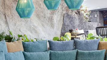 Ein moderner Lounge-Bereich mit einer Steinwand, einem beigen Sofa mit blauen Kissen und einem runden Tisch mit einer Glasvase.