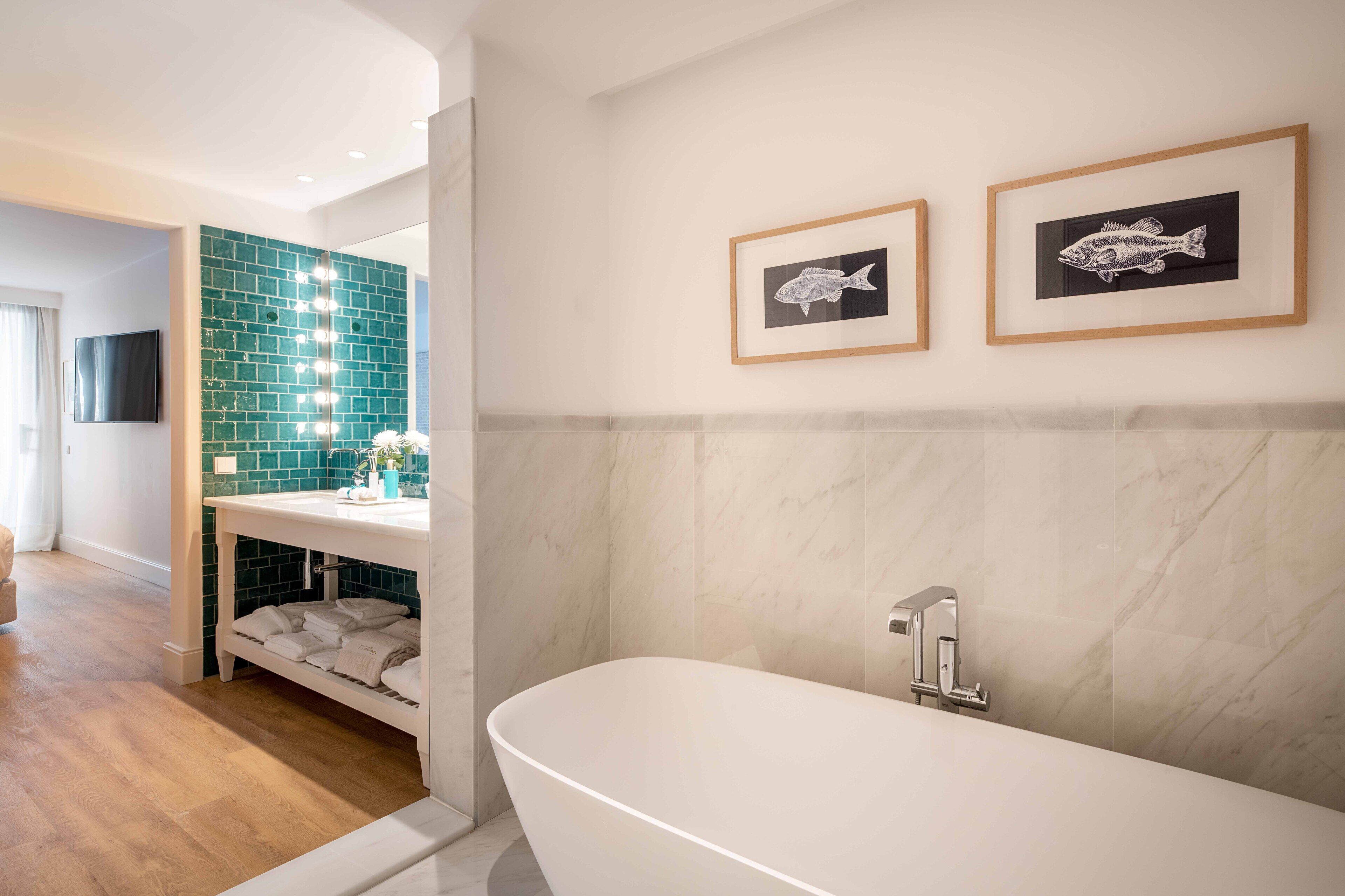 A modern bathroom with a freestanding bathtub, a vanity with a mirror, and two framed fish wall art pieces.