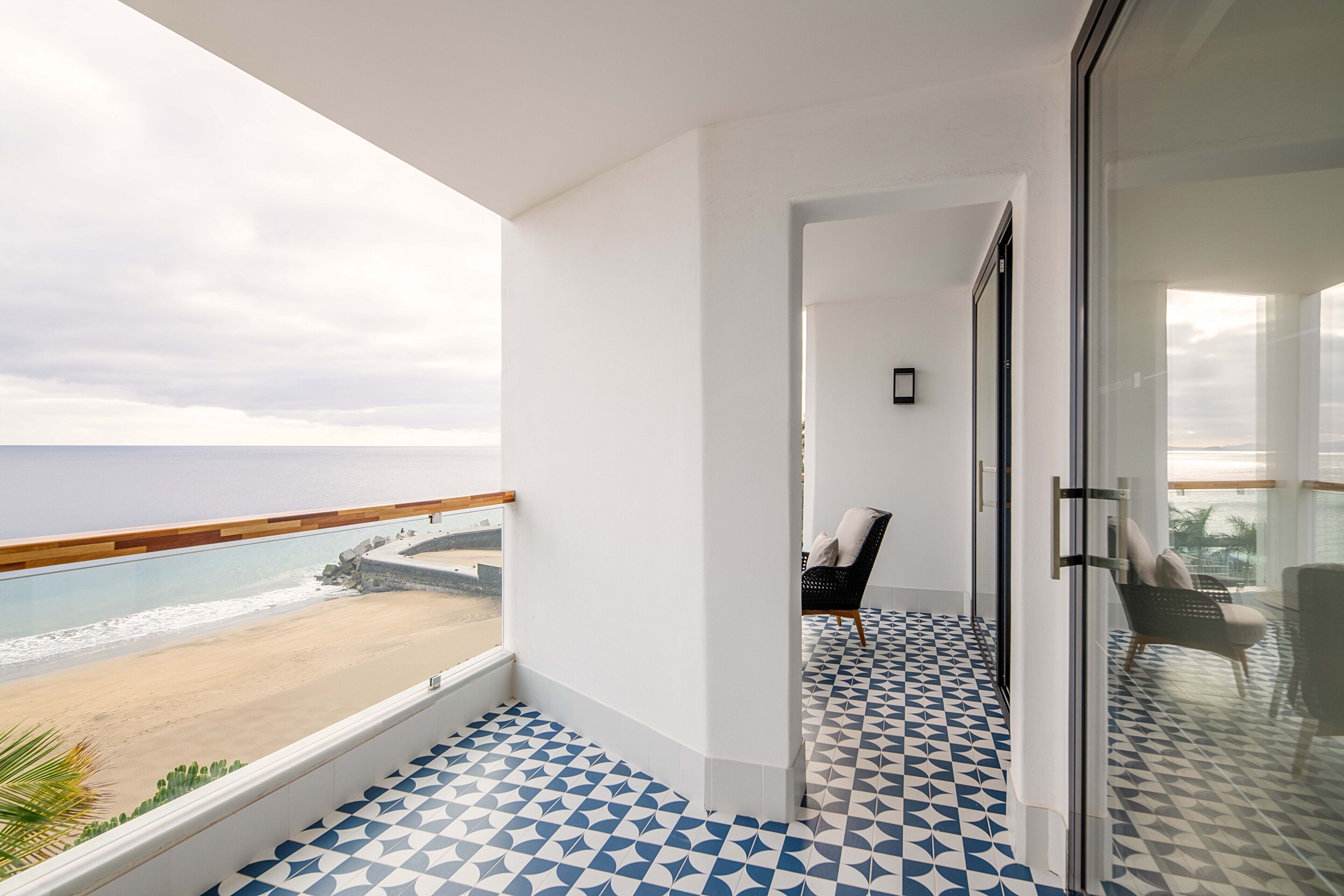 Un balcón con piso estampado, una silla y vista a la playa.