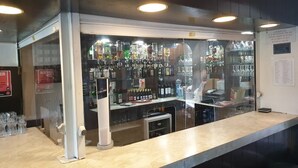 A bar area with a counter, shelves of liquor bottles, and a glass display case. - Elmhurst Hotel (Reading)
