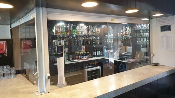 Zona de bar con mostrador, estantes llenos de botellas de licores y una vitrina de vidrio.
