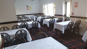 Comedor con varias mesas y sillas, un letrero de salida de incendios y un cartel de prohibición de fumar.