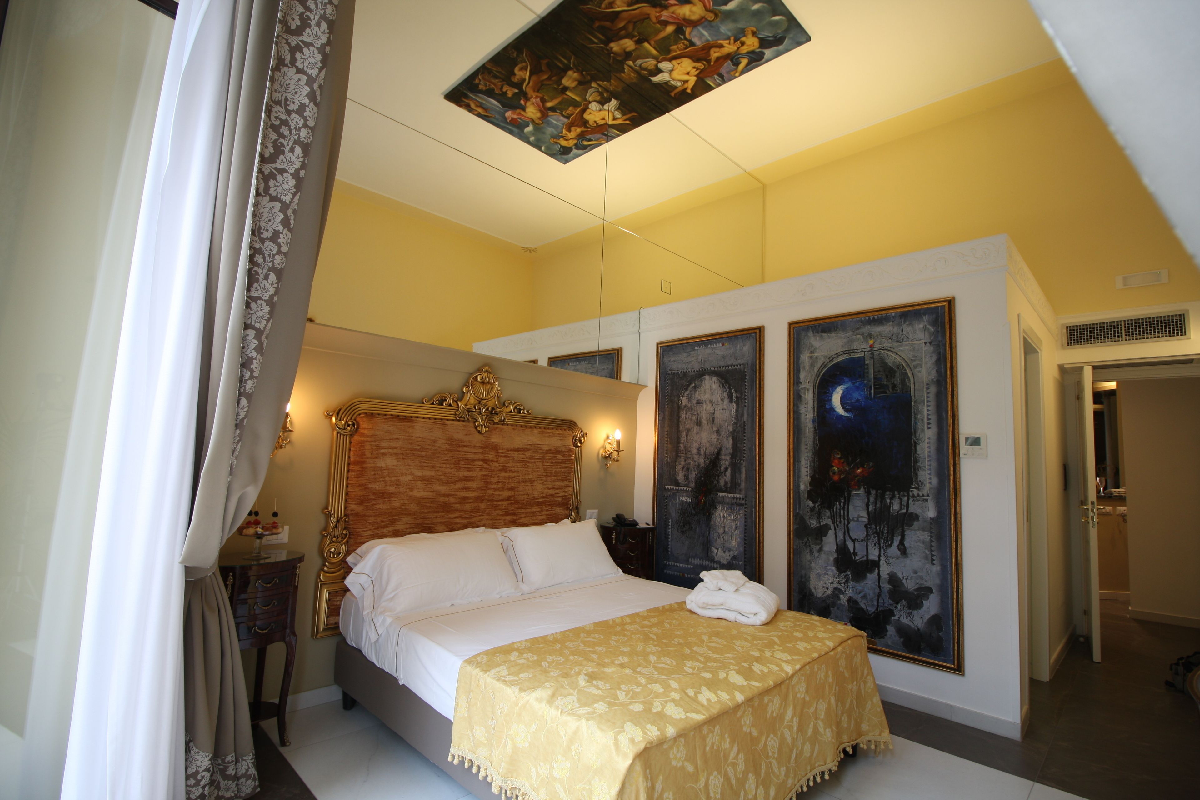 Une chambre à coucher avec un grand lit, une table de chevet, une commode et deux grandes peintures au mur.