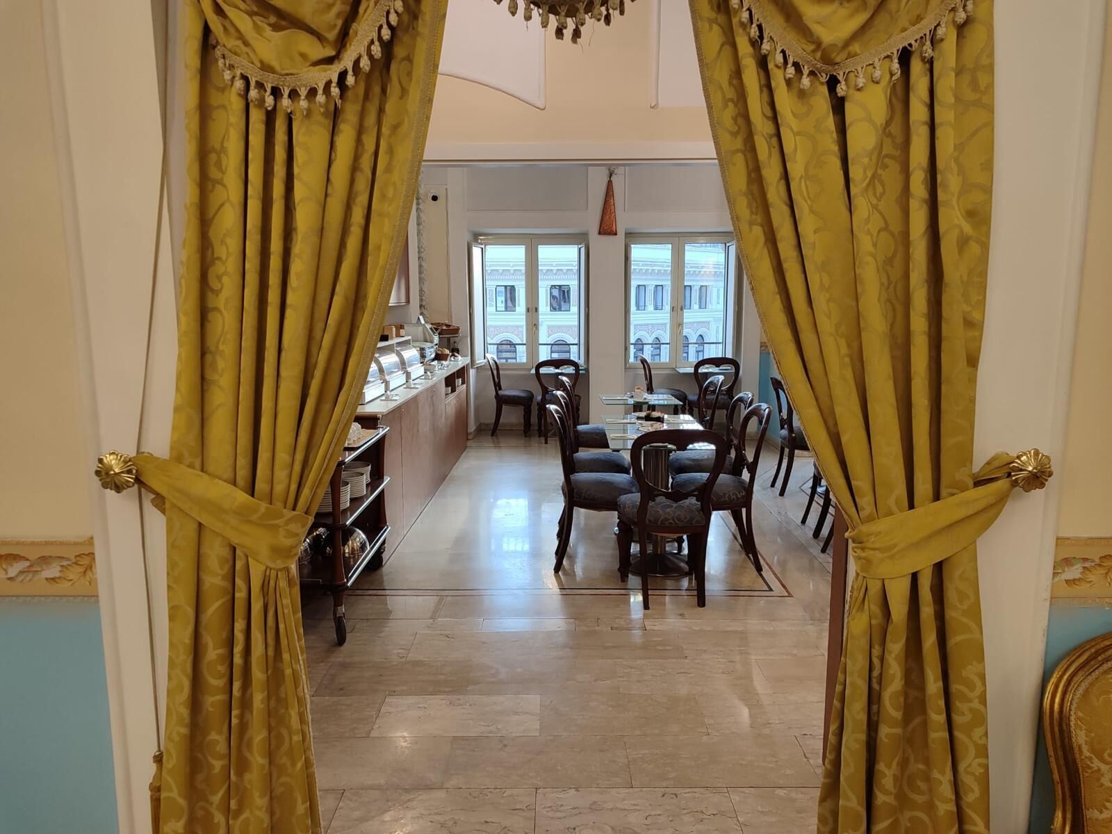 Angolo ristoro con buffet, sedie e vista sugli edifici attraverso ampie finestre.