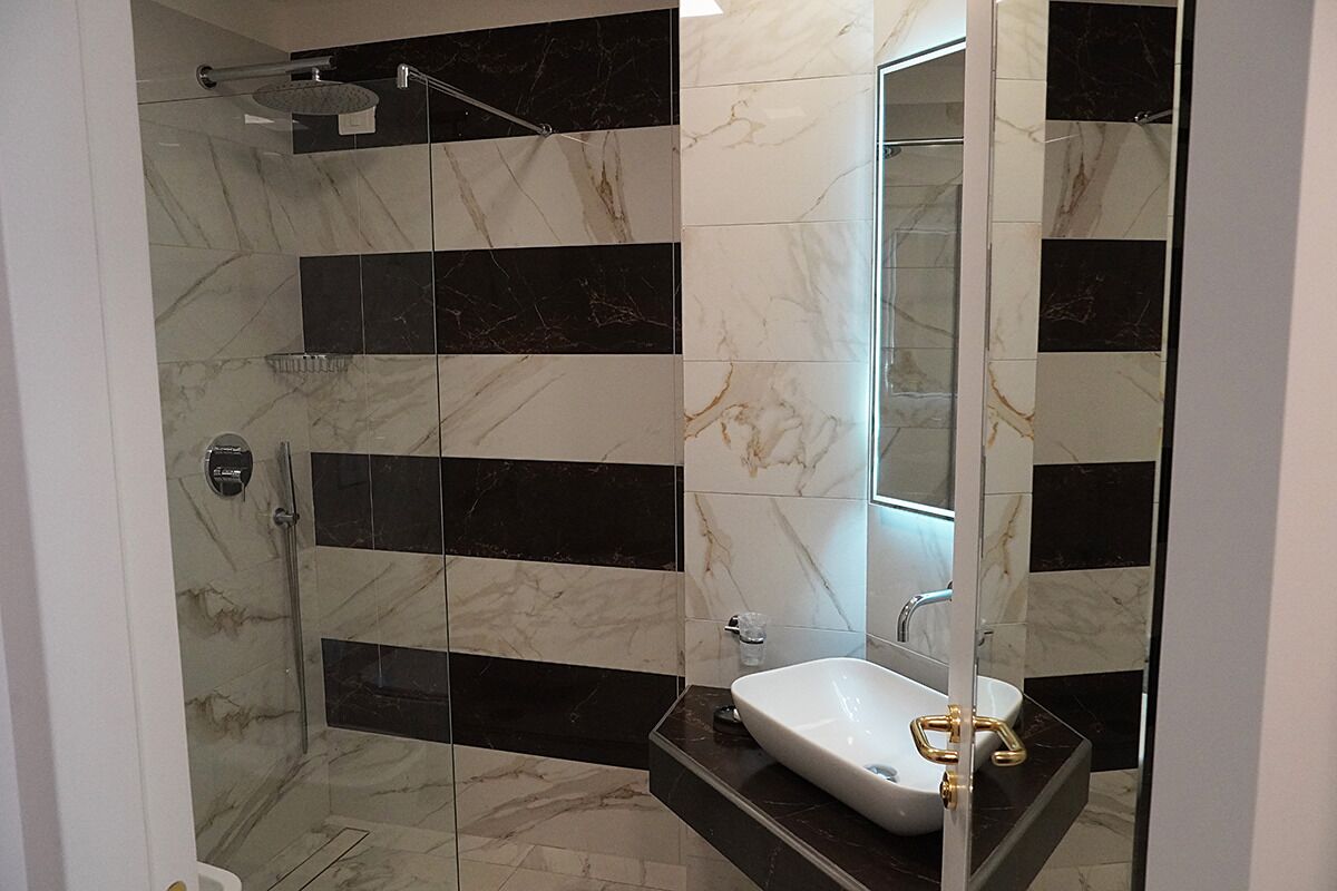 Un baño moderno con ducha envuelta en vidrio, un lavamanos blanco con detalles dorados y un espejo grande.