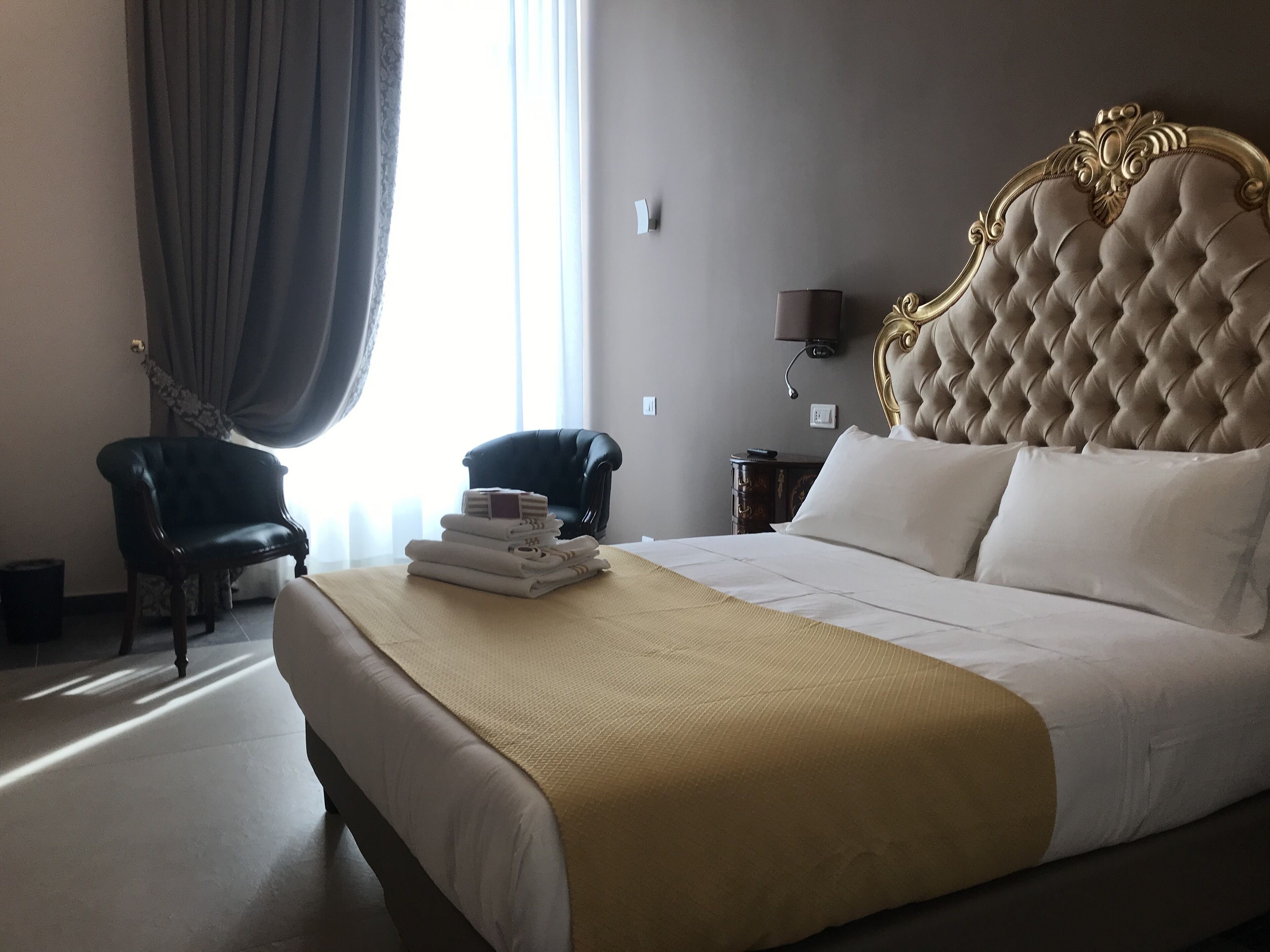 A hotel room with a large bed, two chairs, a bedside table, and a lamp.