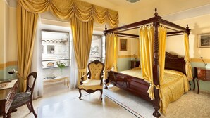 A four-poster bed with a canopy, a wooden chair, a desk with a chair, and a view of a building through a window. - Hotel Art Resort Galleria Umberto (Naples)