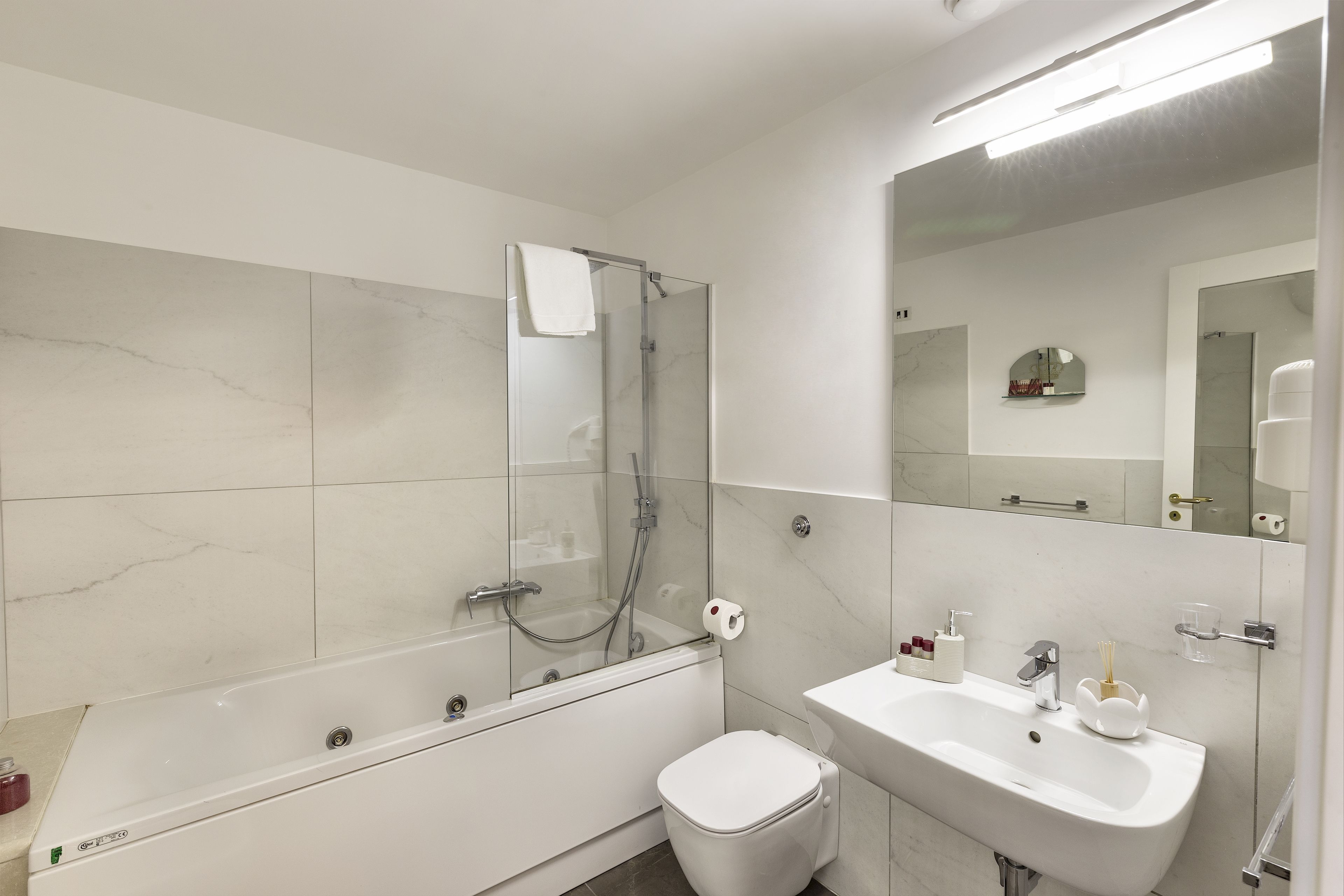 Un baño moderno con ducha envuelta en vidrio, inodoro blanco y lavamanos con espejo.
