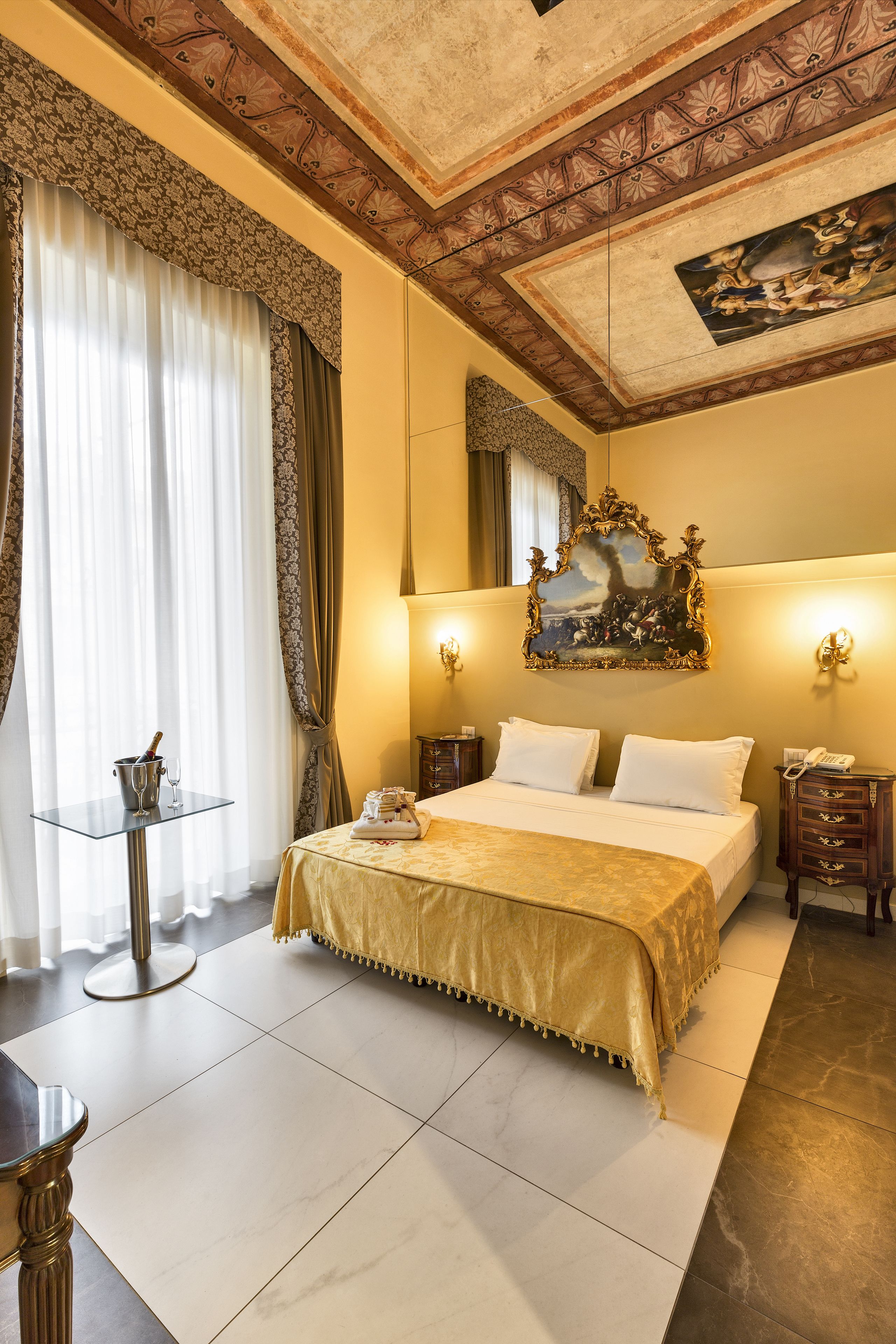 A hotel room with a large bed, a small table with a drink and glass, a telephone, and a painting on the wall.
