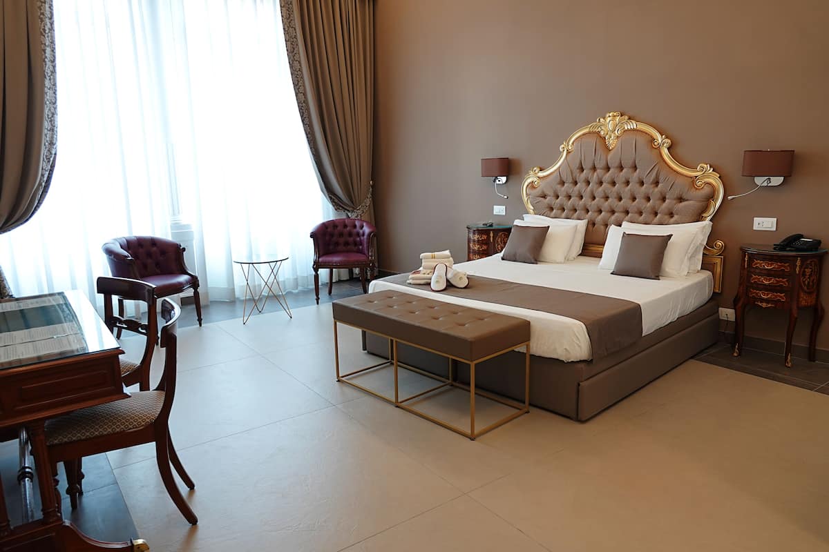 A hotel room with a large bed, a desk with a chair, a small table, and two armchairs.