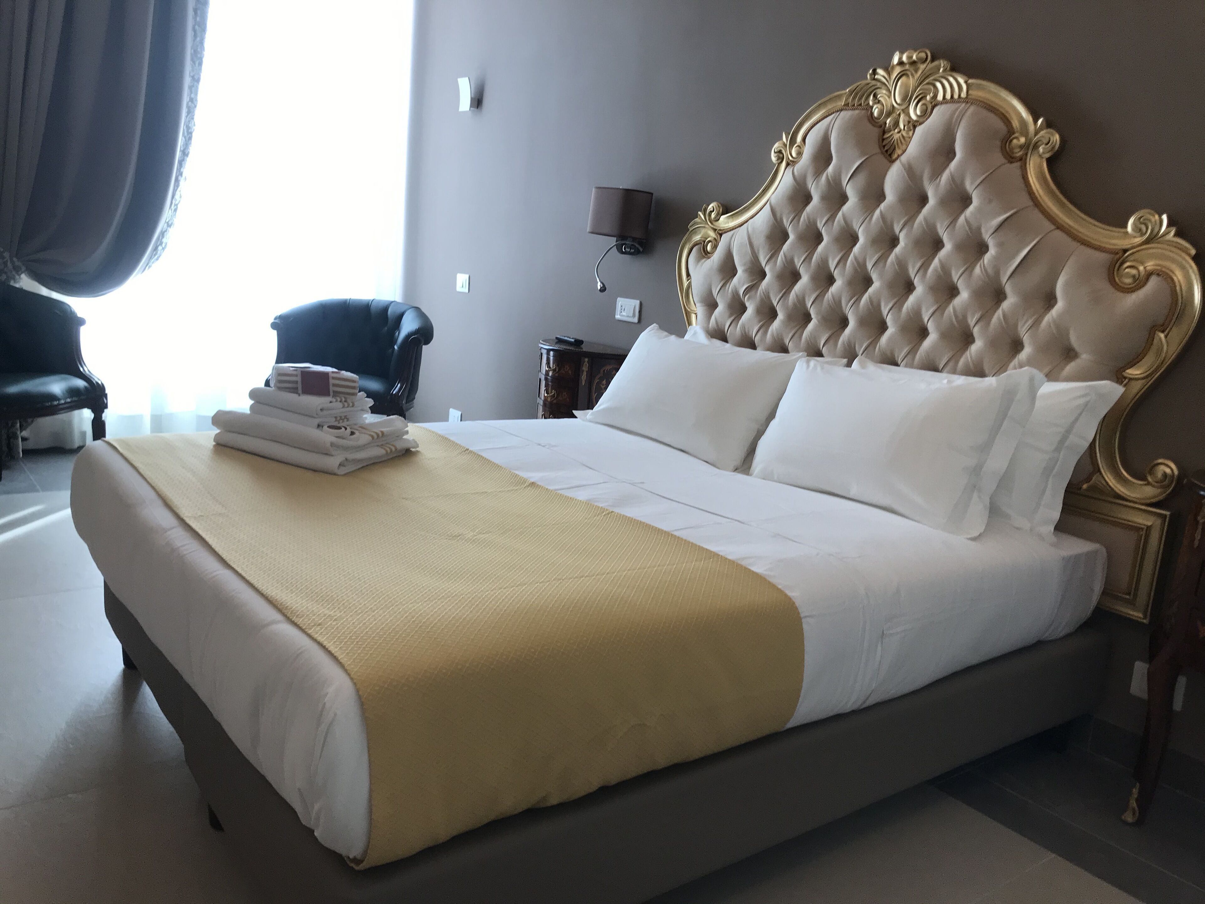 A neatly made bed with a gold-trimmed headboard, white linens, and a folded towel stack.