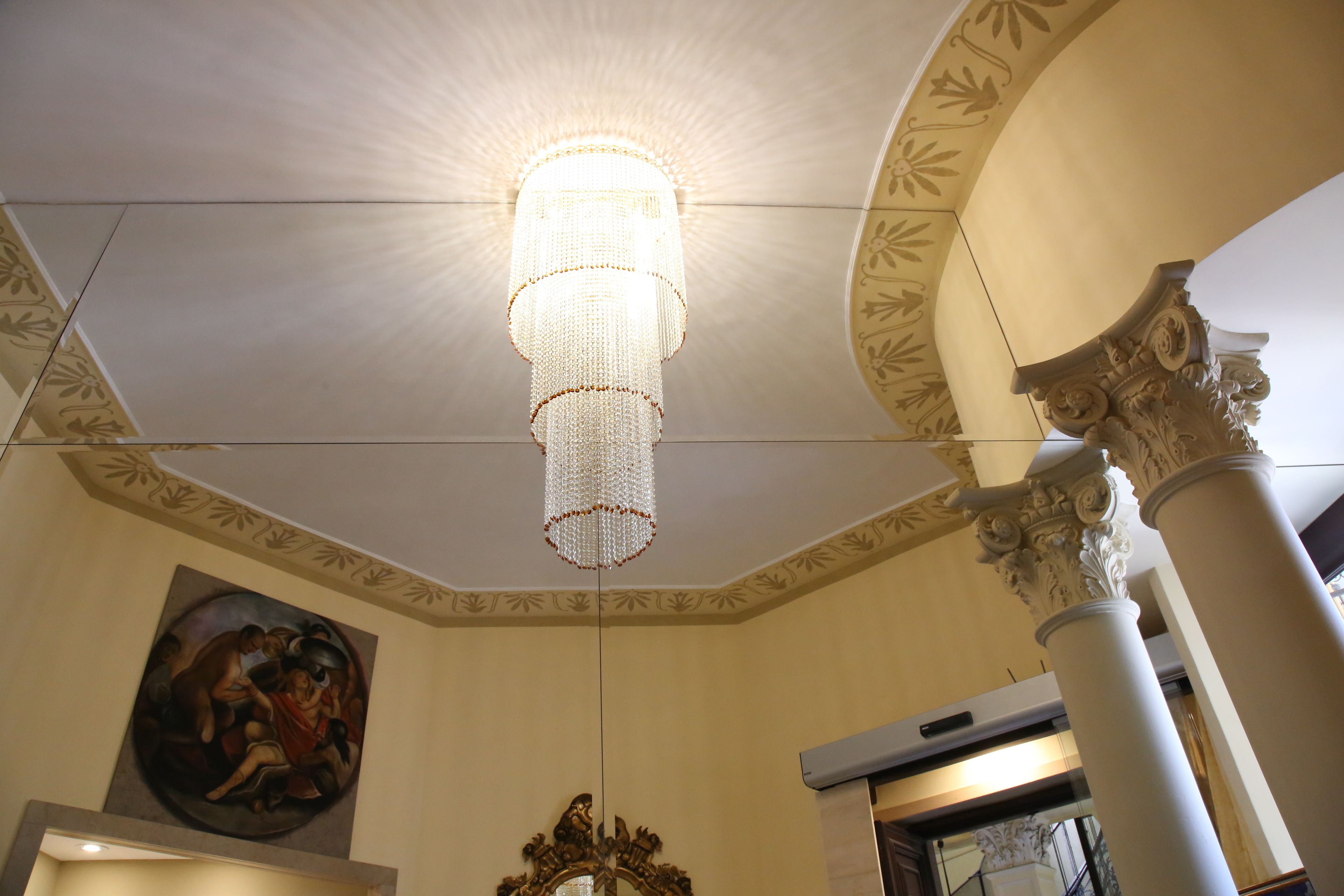 Un lampadario, un dipinto e colonne decorate in una stanza.