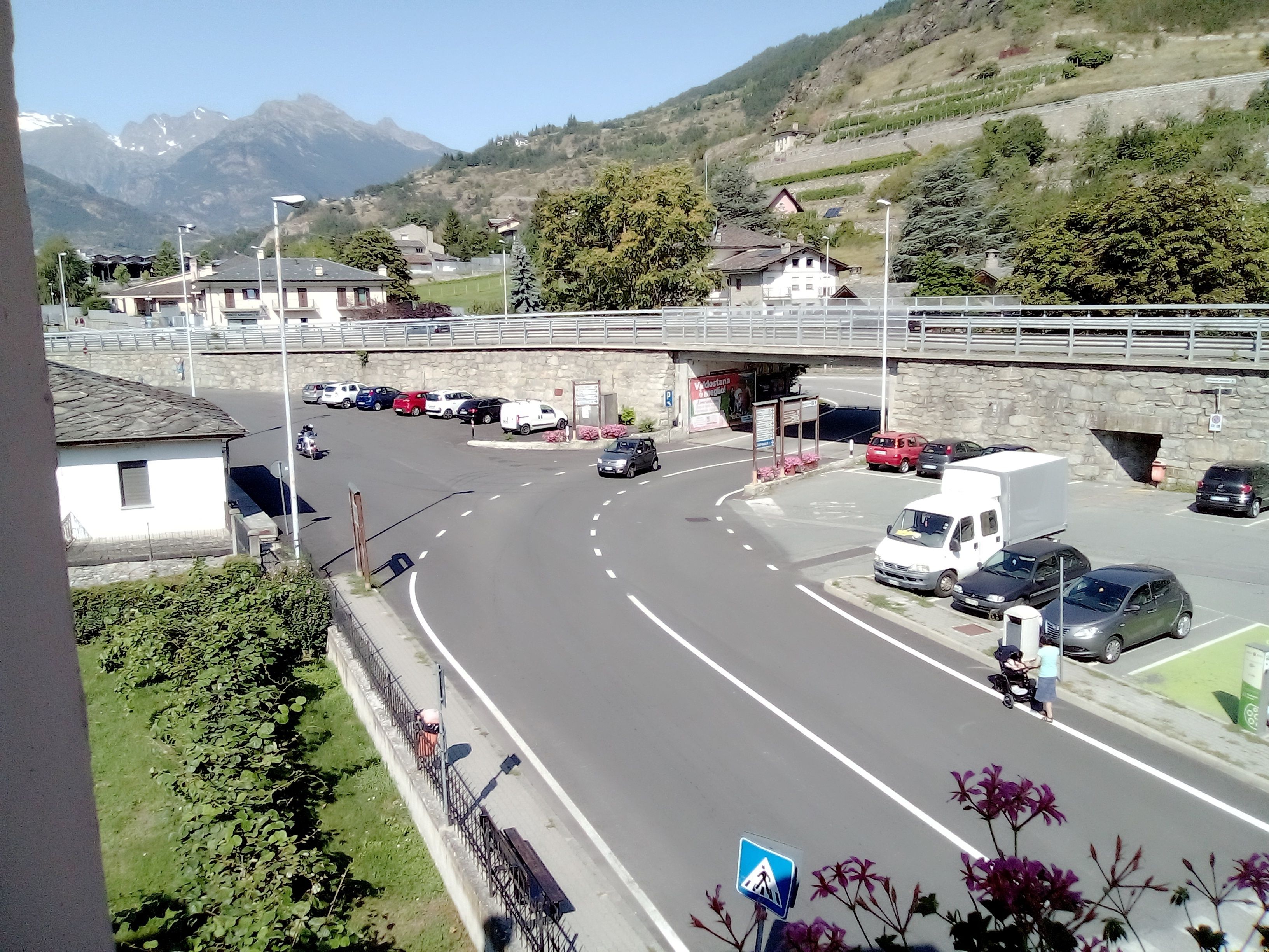 A road with vehicles, a pedestrian crossing, and a stone bridge.